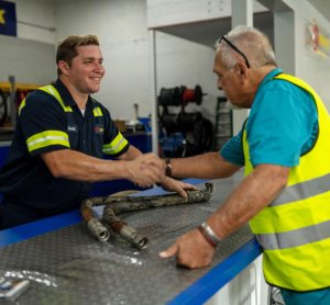 Two male workers in safety vests shaking hands over a workbench in a hydraulic franchise workshop in Baltimore, MD.